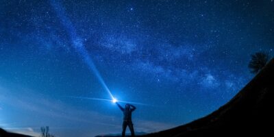 Silhouette of man holding flashlight against blue, starry night sky