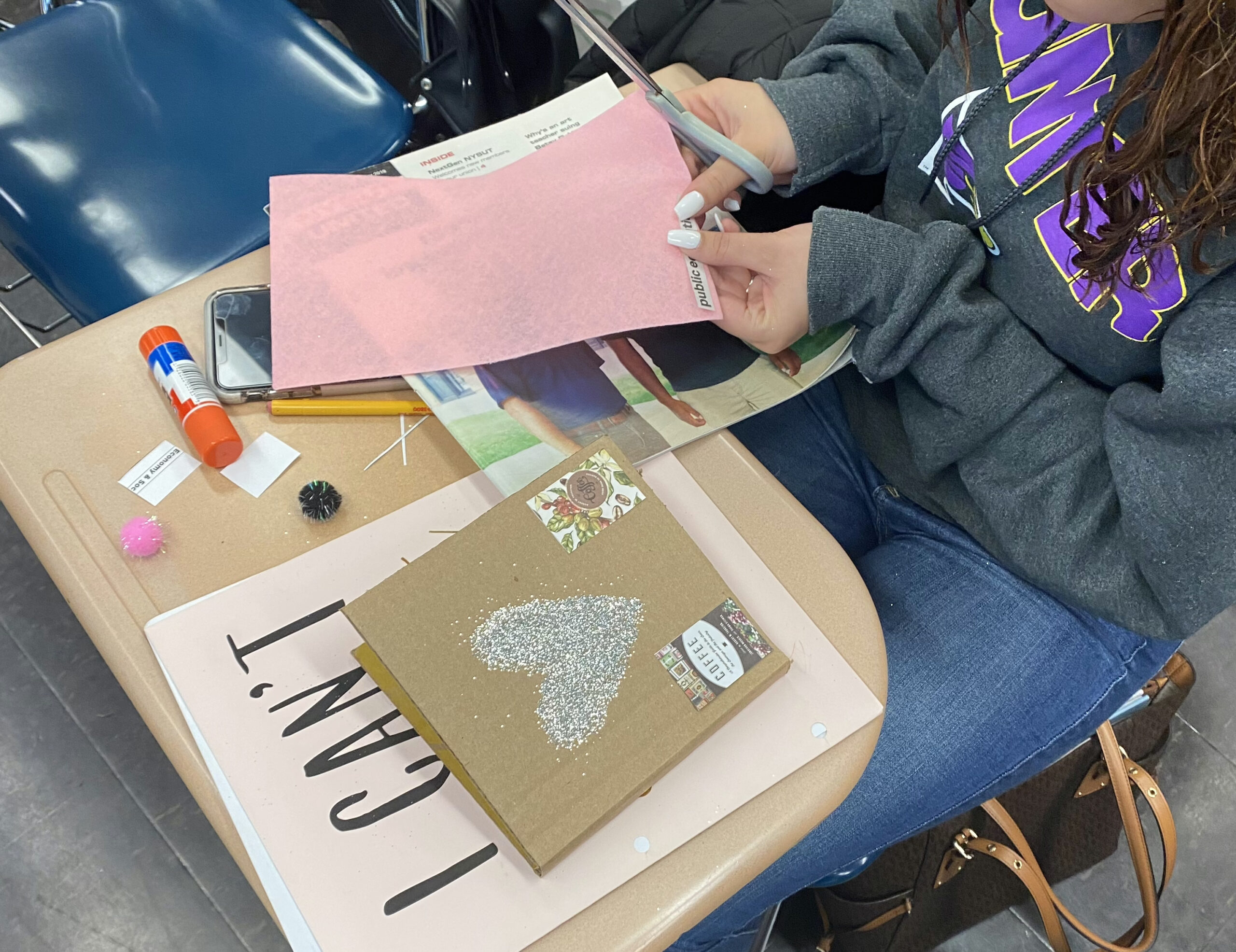 A student cuts pink tissue paper to add to a cartonera book in progress. The cover is plain cardboard with a silver glitter heart