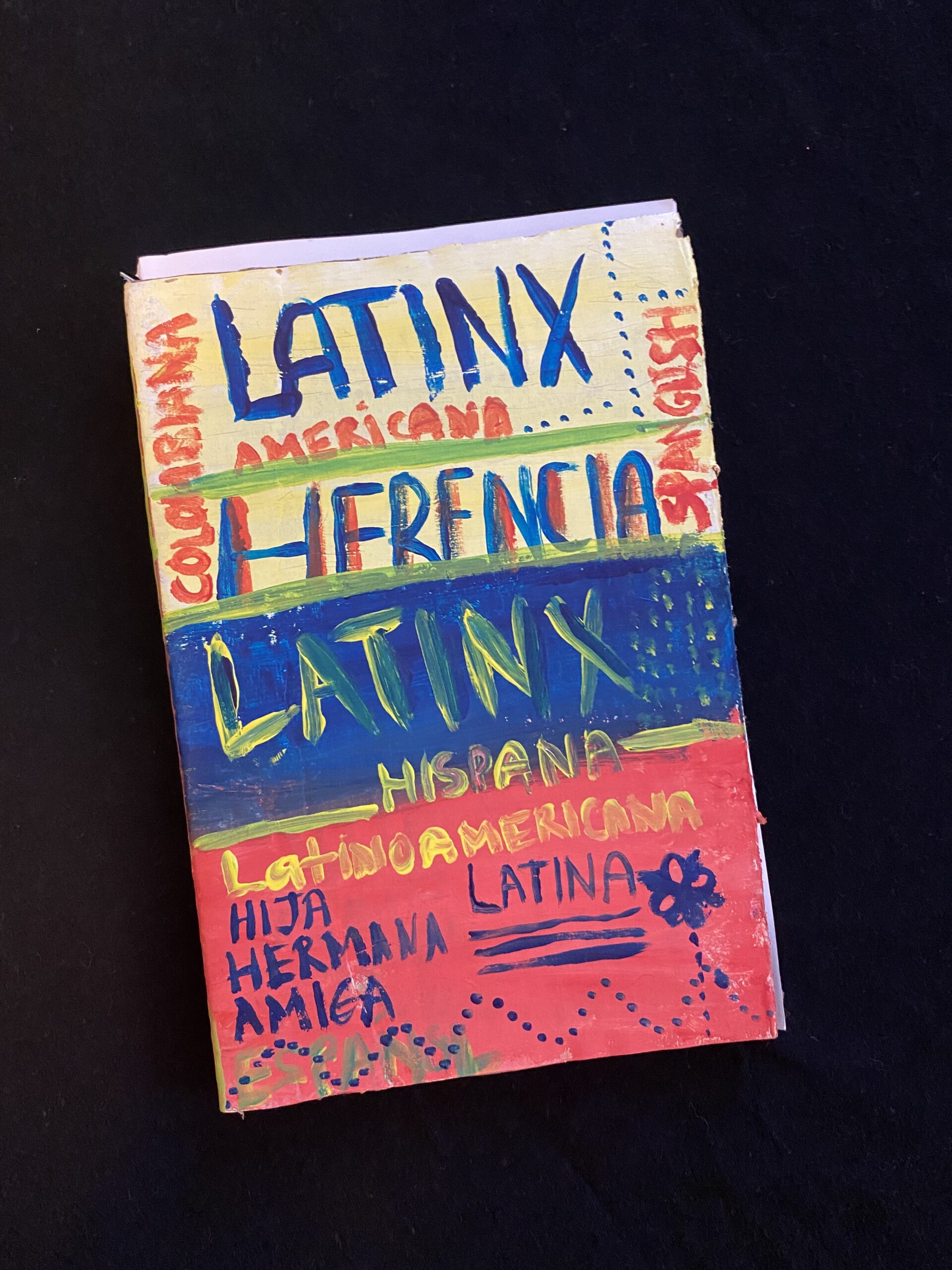 hand-painted cartonera book with horizontal bands corresponding to the Colombian flag--yellow, blue, red--that reads "Latinx Herencia"