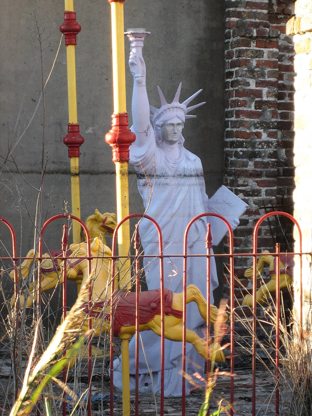 a white replica of the Statue of Liberty stand behind a metal fence with a receded water line at the chest.