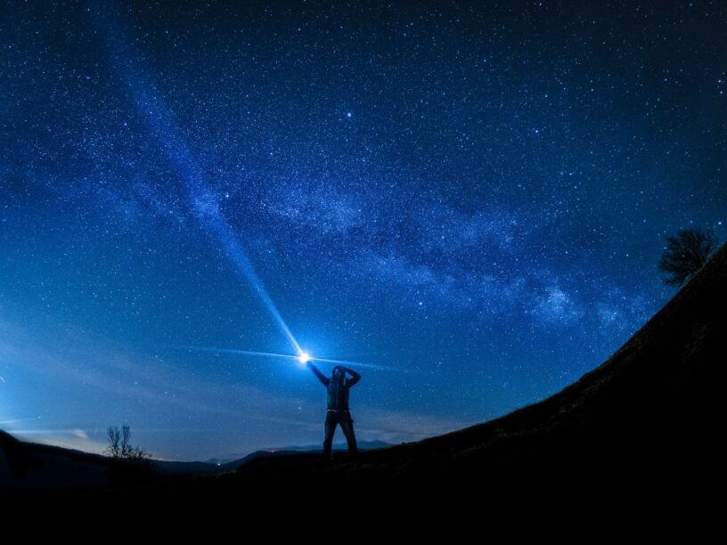 Silhouette of man holding flashlight against blue, starry night sky