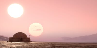 Desertscape of Tatooine, with two suns set against a pink sky, hut in the foreground on the left side of the image.